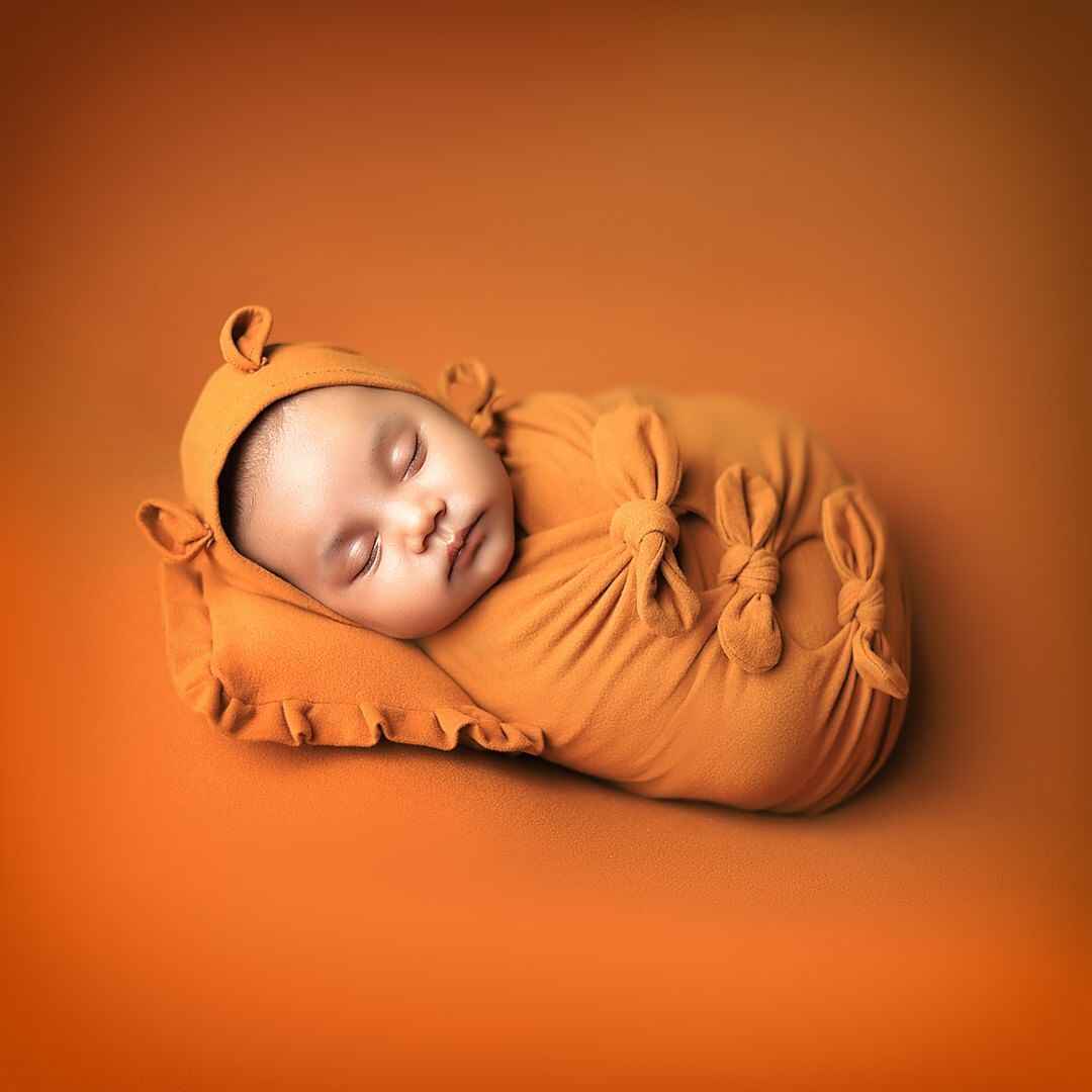 A newborn baby girl cuddled in a cozy mustard outfit, peacefully sleeping in a magical baby photography session.